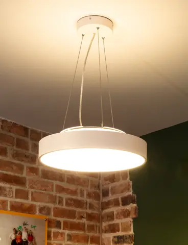 A round, white pendant light in front of a wall that is partly brick and partly dark green
