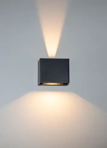 A luminous black wall light with beams of light directed upwards and downwards at various angles