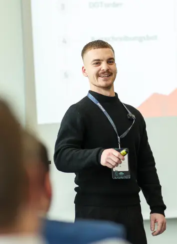 A group of athletic participants after a competition, some wearing medals and smiling proudly into the camera. Trees and event tents in the background.