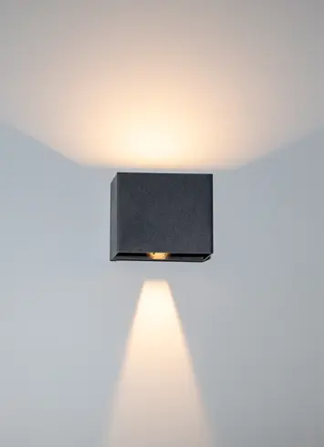 A luminous black wall light with beams of light directed upwards and downwards at various angles