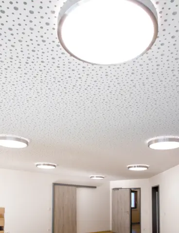 A round, white ceiling light providing direct and indirect lighting on a white ceiling