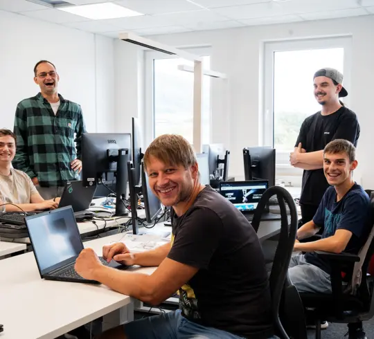 Eine Gruppe von Mitarbeitern stehend und sitzend an Bürotischen in einem Büro