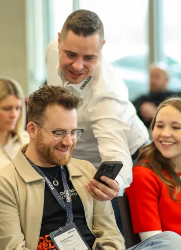 A group of cheerful people standing in an office and cheering into the camera.