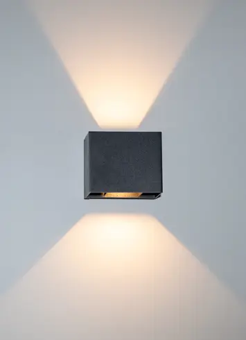 A luminous black wall light with beams of light directed upwards and downwards at various angles