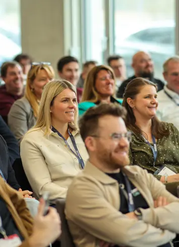 A group of athletic participants after a competition, some wearing medals and smiling proudly into the camera. Trees and event tents in the background.