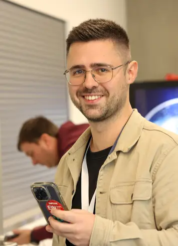 A group of athletic participants after a competition, some wearing medals and smiling proudly into the camera. Trees and event tents in the background.