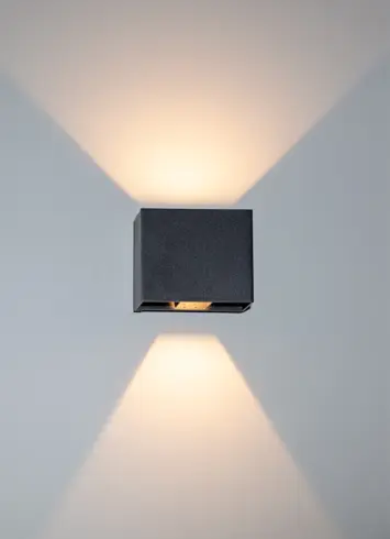 A luminous black wall light with beams of light directed upwards and downwards at various angles