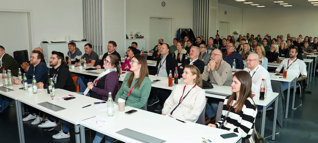 A man and a woman laugh heartily as they sit at a coffee machine in a modern kitchen.
