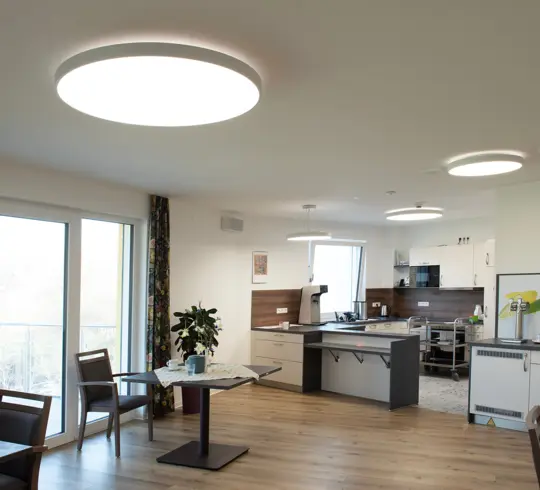 The common room of a care home with large, round lights on the ceiling