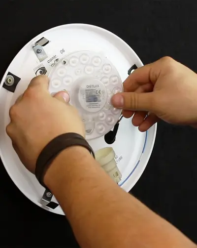 A round ceiling light, suspended from a metal support, emits bright light. The lamp is located in an industrial setting with visible supports and a functional design.