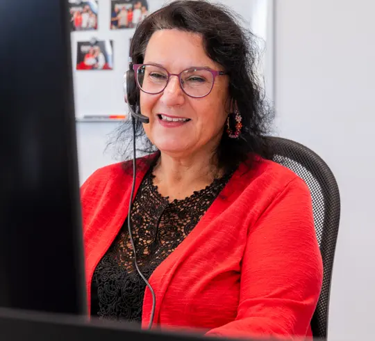 Eine Frau mit langen dunklen Haaren sitzt mit Headset an einem Schreibtisch und telefoniert