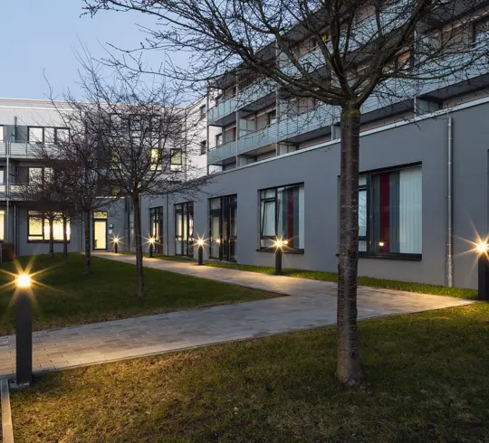 A hospital garden at dusk, with the path lights switched on