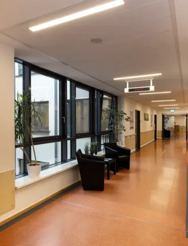 Ein Flur im Krankenhaus mit Fensterfront, Sitzecke und Beleuchtung an der Decke